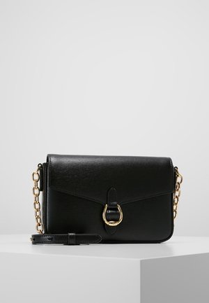 Musta nahkainen olkalaukku, jossa kullanvärinen ketjuhihna ja kultainen solkikoriste, asetettuna valkoiselle pinnalle yksiväristä harmaata taustaa vasten.