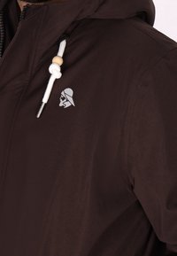 Veste à capuche marron avec un logo argenté, des cordons blancs agrémentés d'une perle en bois, et un tissu lisse et texturé.