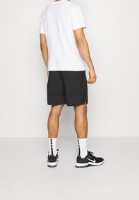 Vit t-shirt med kort ärm, svarta träningsshorts, svarta och vita sneakers, samt vita strumpor med svarta ränder, sedd bakifrån.