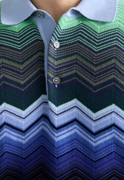 Polo tricotat cu un model în zigzag în nuanțe de verde, albastru și violet. Guler scurt cu două butoane, design cu textură.