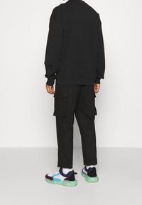 Sweat-shirt noir surdimensionné, pantalon cargo ample et baskets multicolores avec une semelle épaisse verte. Tissu lisse et coupe décontractée.