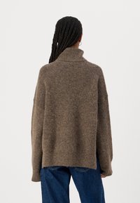 Maglione marrone, oversize, con collo alto, realizzato in un tessuto morbido e testurizzato. Presenta spalle calate e una vestibilità rilassata.