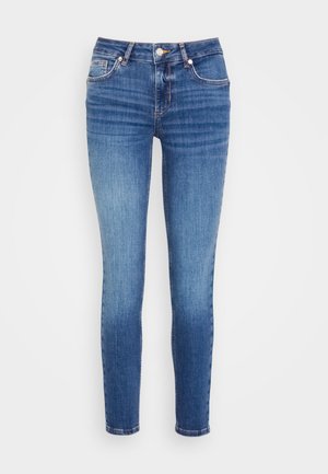Kitsas teksad keskmises sinises denimis, millel on kerge pleekimine. Omab viit taskut, nööri ja lukuga kinnitust ning õmblusaktsente õmblustes.