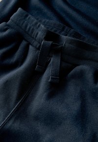 Tummansinisiä verkkareita, joissa on ribbikuvioitu elastinen vyötärö, jossa on naru. Kangas on pehmeää ja sileää ilman näkyviä kuvioita.
