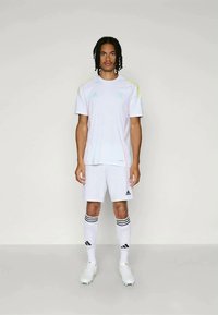 Maillot de sport blanc avec des accents clairs, accompagné de shorts assortis, de chaussettes jusqu'aux genoux avec des rayures noires, et de crampons de football.