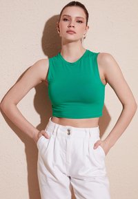 Zelený, priliehavý crop top s okrúhlym výstrihom a bezrukávovým dizajnom, skombinovaný s bielo vysokým pásom nohavicami s dvojitým gombíkovým zapínaním.