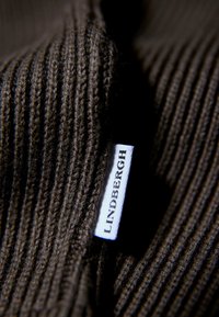 Tejido de punto acanalado marrón con una textura suave y una etiqueta blanca que dice "LINDBERGH" unida al borde.