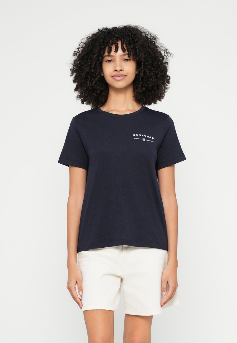 Tmavomodré bavlnené tričko s krátkymi rukávmi, okrúhlym výstrihom a bielym nápisom "GANT 1949" vytlačeným na hrudi.