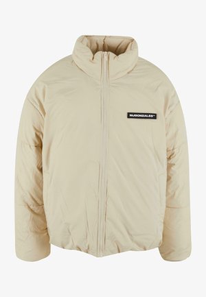 Beige puffer jacket with high collar, zip closure, and black logo patch on the left chest. Features quilted texture and loose fit.