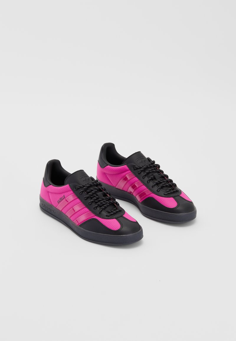 Tenis pretos e cor-de-rosa com parte superior em malha, sola de borracha e atacadores pretos. Apresenta três riscas cor-de-rosa de lado e um design de bico arredondado.
