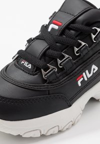 Sorte lær sneakers med teksturert overflate, hvit gummisåle, metall snørehaker og rød/hvit logoaksel på siden.