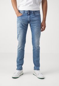 Ljusblå denimjeans med slim fit, femficksdesign och synliga sömnadsdetaljer. Bärs med en vit T-shirt och vita sneakers.