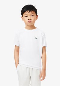 White cotton t-shirt with short sleeves, crew neck, and small green embroidered crocodile logo on the left chest. Simple and classic design.