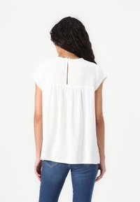 White blouse with short sleeves, round neckline, and keyhole detail at the back. Features textured trim and a relaxed fit design.
