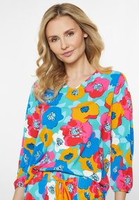 Farverig blomstret bluse med V-hals, med store blomstermønstre i blå, pink, gul og hvid. Lavet af letvægtsstof, trekvartærmer.