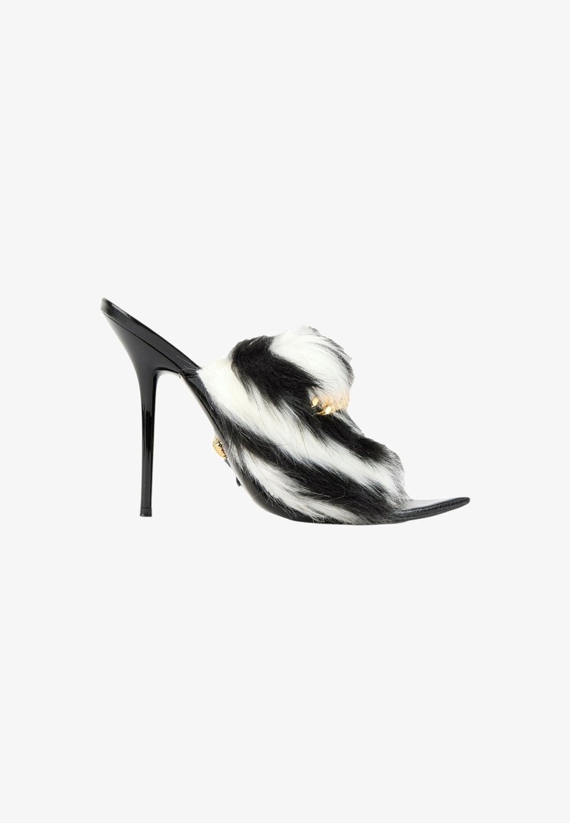 Mule à talon stiletto noire avec des brides en fourrure noire et blanche et petits détails en chaîne dorée sur fond blanc.