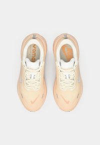 Adidași de alergare de culoare piersici deschis, cu un upper texturat, accente albe, guler căptușit și un swoosh Nike reflectorizant de culoare argintie.