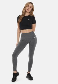 Čierny skrátený športový top a šedé legíny s vysokým pásom s jemným melírovaným vzorom. Obe majú malé biele logo. Čierne tenisky.
