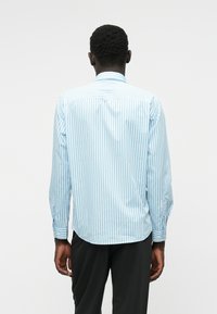 Camicia con bottoni, maniche lunghe, a righe verticali blu chiaro e bianche, orlo arrotondato e polsini con bottoni. Tessuto morbido in misto cotone.