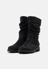 Svarta mocka ank stövlar med en slouchy design, rund tå, lätt texturerad sula och subtila sömdetaljer längs sidorna.