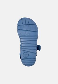 Sininen kuminen kenkäpohja, jossa on teksturoitu pito, ja jossa on ympyrän muotoinen logo ja brändin nimi 'COMOD.' kohokuvioituna. Kaareva muotoilu, jossa on uria.