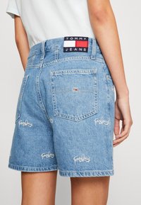 Ljusblå denimshorts med hög midja, broderade "Tommy Jeans"-logotyper och en märkeslapp på baksidan av midjan.