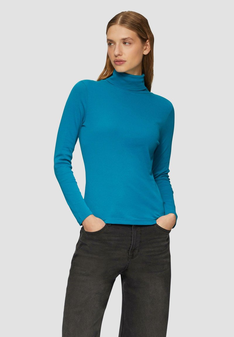 Turquoise coltrui gemaakt van een zachte, rekbare stof met lange mouwen, gecombineerd met donkergrijze jeans. Glad textuur, aansluitend ontwerp.