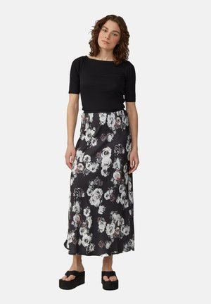 Schwarzes kurzärmliges Oberteil kombiniert mit einem langen, floralen Rock, der weiße und rosa Rosen auf einem schwarzen Hintergrund zeigt. Dicke schwarze Plateau-Sandalen.