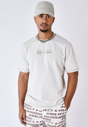 Camiseta corta de manga gris claro con detalles de costura y el logo de "Project x Paris", combinada con pantalones cortos estampados en tonos blancos y marrones.