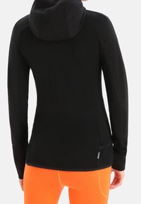 Felpa nera a maniche lunghe con cappuccio aderente, dotata di cappuccio e tasche laterali, abbinata a pantaloni aderenti di un arancione brillante.