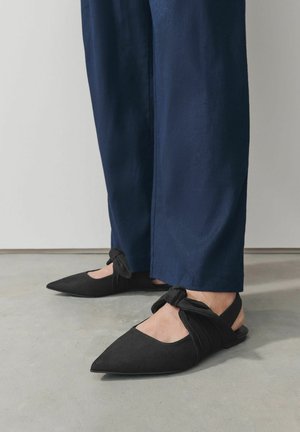 Mustat nappa-slingback-kengät, joissa on terävä kärki, solmittu hihnatieto ja matala profiili. Yhdistettynä tummansinihin housuihin.