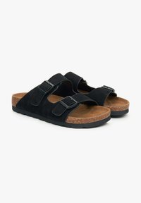 Zwarte suède slide sandalen met twee verstelbare banden en metalen gespen, voorzien van een bruine kurken voetbed en een zwarte rubberen zool.