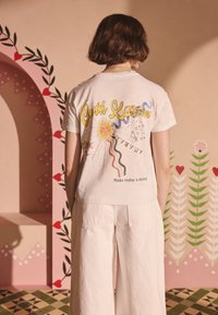 Biele tričko s krátkymi rukávmi a farebným grafickým dizajnom so slnkom, hviezdami a textom „Make today a story“ na zadnej strane. Pohodlný strih.