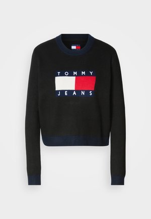 Maglione nero a maniche lunghe e collo rotondo, con una patch logo blu, bianca e rossa che riporta la scritta "TOMMY JEANS" sul davanti.