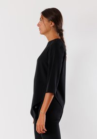 Top nero a tre quarti con scollo rotondo, caratterizzato da un orlo curvo e un tessuto liscio e strutturato. Design slim fit mostrato di lato.