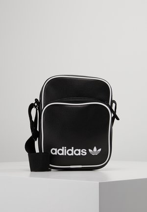 Sort Adidas crossbody-taske med hvid kant, lynlås foran, justerbar rem og hvid Adidas-logo på frontlommen.