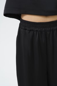 Svart idrottstopp med en kortad design, kombinerad med svarta shorts med elastisk midja. Båda är tillverkade av ett glatt, lätt material med en glänsande yta.