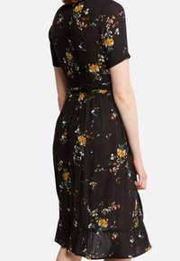 Černé květinové šaty s krátkými rukávy, zdobené barevnými květinovými vzory, s páskem v pase a volánkovým lemem nad koleny. Texturovaná látka.