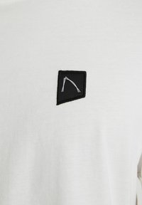 Biela tričko s čiernym vyšívaným logom a geometrickým dizajnom. Hladká štruktúra a štýl s okrúhlym výstrihom.