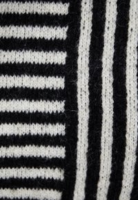 Tessuto lavorato a maglia nero e crema con strisce spesse e sottili alternate, caratterizzato da una texture morbida e schemi variabili in tutto il tessuto.
