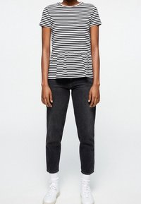 Svart och vit randig kortärmad topp med peplummidja, kombinerad med svarta jeans och vita sneakers. Enkelt, avslappnat design.