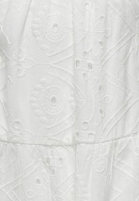 Bijela tkanina s teksturiranom izvezenom vrstom koja sadrži kružne i cvjetne uzorke, male izreze i dizajn s naboranim strukom.