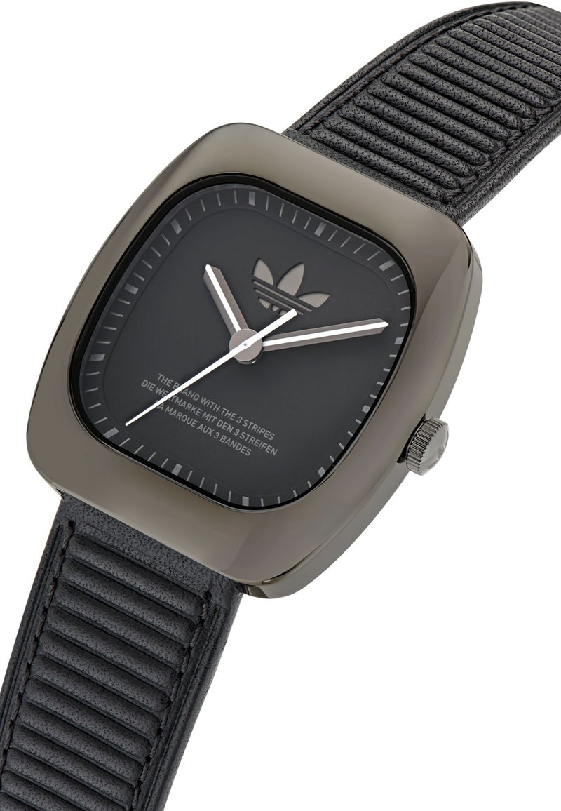 Montre noire en forme de quadrant avec un bracelet en silicone texturé noir. Présente des aiguilles des heures et des minutes argentées, ainsi qu'un logo en relief sur le cadran.
