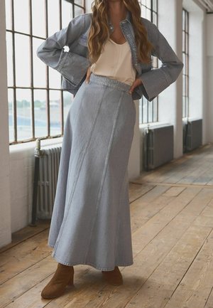 Giacca di jeans azzurro chiaro con tasche a pattina abbinata a una gonna lunga coordinata, caratterizzata da cuciture verticali e stivali alla caviglia marroni.