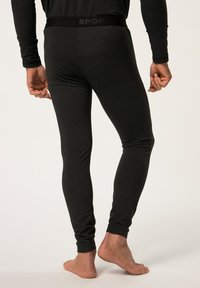 Schwarze Sportleggings mit enger Passform, die eine glatte Textur und einen markierten Bund aufweisen. Lockere Bündchen an den Knöcheln.