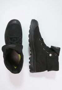 Bottes en toile noires avec une semelle en caoutchouc, à bout rond et à laçage. Equipées d'un col rembourré et d'une étiquette à la cheville. Finition texturée remarquable.