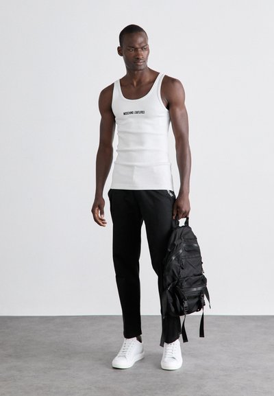 Top alb fără mâneci cu text negru logo, combinat cu pantaloni negri și un rucsac negru. Încălțămintea constă în adidași albi. Design simplu, stil casual.
