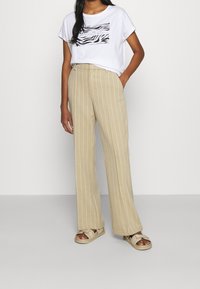 Camiseta gráfica blanca con diseño de rayas negras, combinada con pantalones de pierna ancha de rayas verticales beige y sandalias claras.