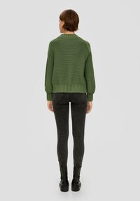 Groen gebreid sweater met een geribde zoom en boorden, gedragen met donkere skinny jeans en zwarte enkellaarsjes. De textuur lijkt dik en heeft een casual pasvorm.