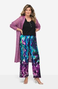 Lila stickad cardigan, svart knäppt topp och vida byxor med färggård abstrakt mönster i blå, grön och lila nyanser. Silverfärgade klackar.